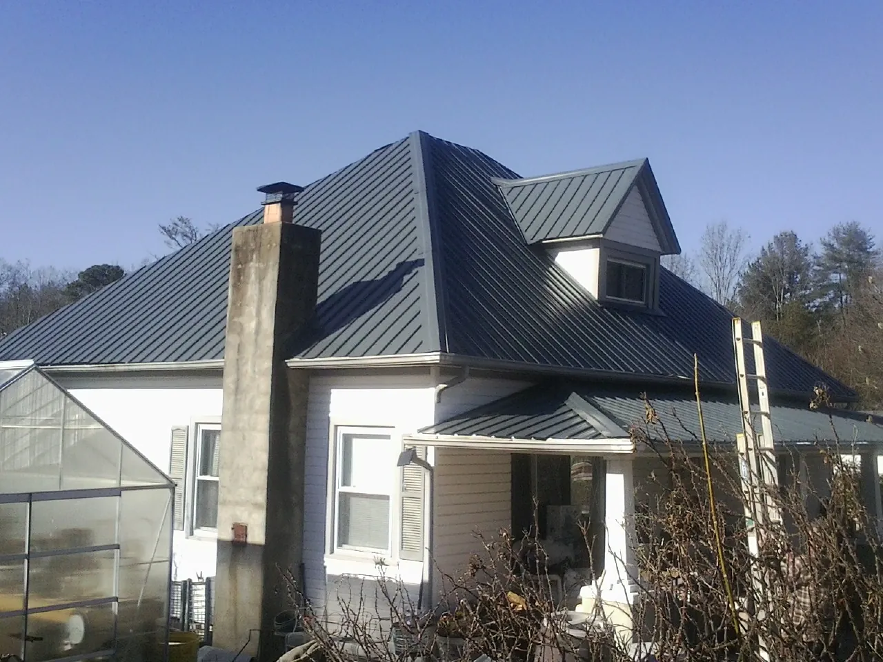 Dark blue standing seam metal roof on a white farmhouse with dormer — Slate & Tile Roof Repair by Roofing Brothers in Pershing