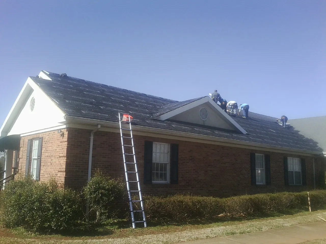 Crew tearing shingles off a brick ranch roof with a ladder set — Metal Roof Repair work by our crew in Pershing