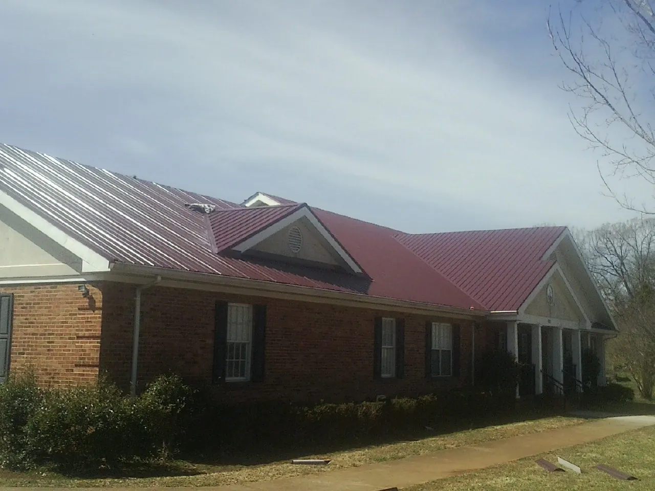 Red metal roof with gabled entries on a long brick building, from a Hail Damage Roof Repair job in Pershing