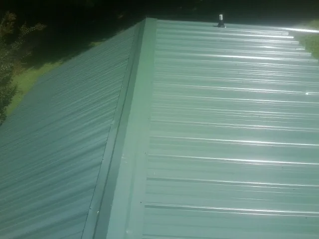 New green metal panels meeting at the ridge of a roof — Flat Roof Repair work by our crew in Pershing
