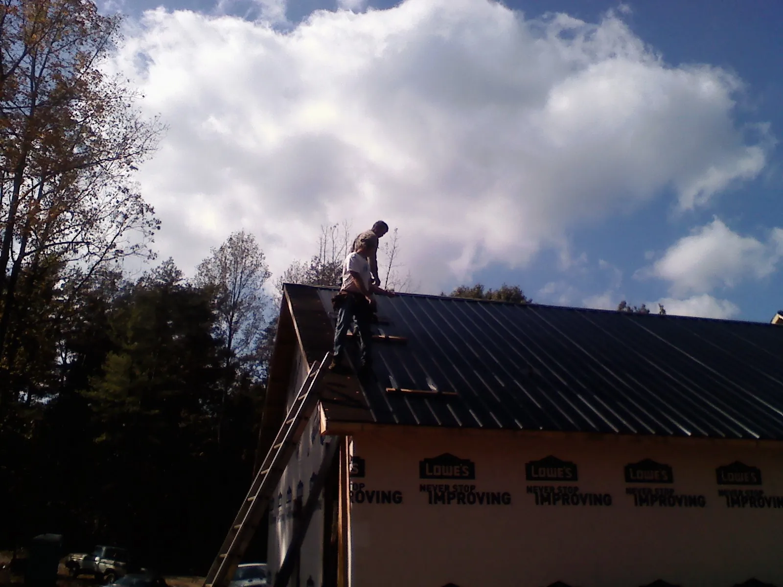 Roofer fastening dark metal panels high against a cloudy sky, from a Roof Inspection job in Pershing